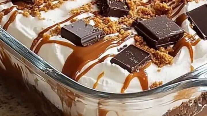 A glass casserole dish with layers of chocolate crust, whipped cream, caramel drizzle, and chocolate chunks.