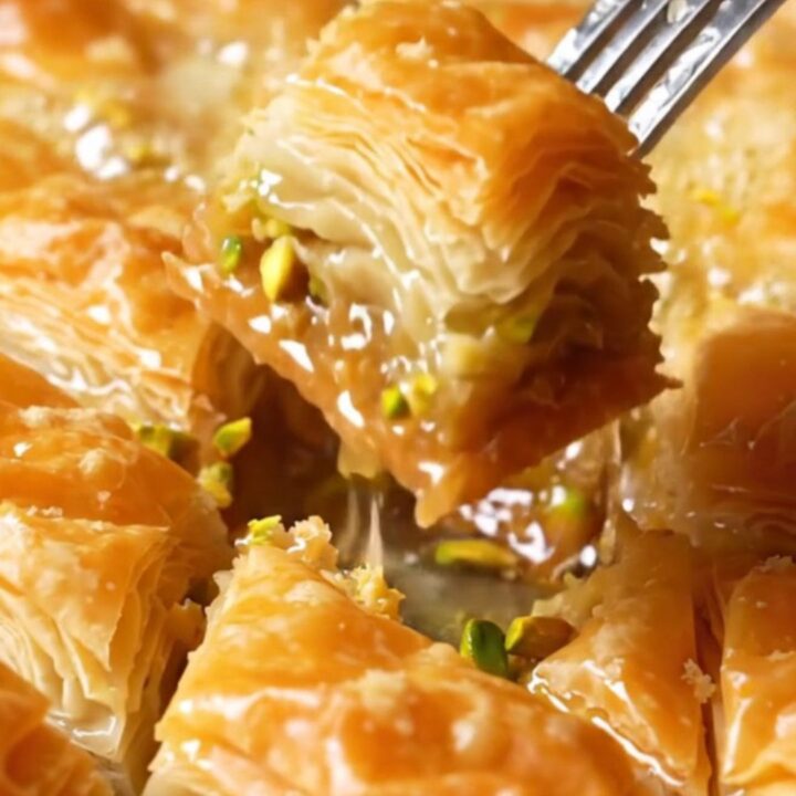 Golden diamond-cut baklava with syrup being poured, showing crispy layers and pistachio filling.