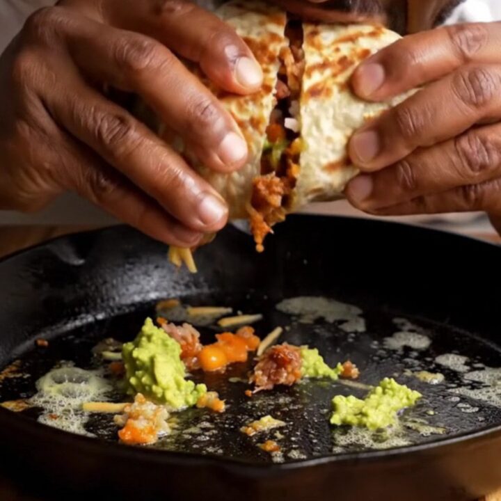Crispy pork carnitas burrito cut in half showing layers of rice, beans, carnitas, guacamole, and cheese
