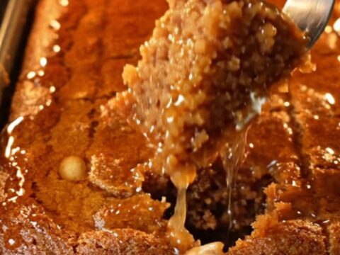 A tray of Turkish Şambali cake with lemon syrup being poured over, peanuts visible on top