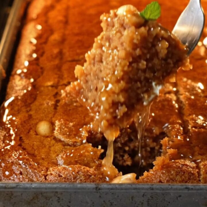 A tray of Turkish Şambali cake with lemon syrup being poured over, peanuts visible on top