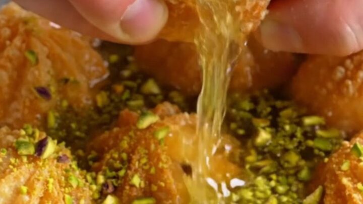Golden fluted tulumba pastries glistening with syrup and topped with crushed pistachios on a plate