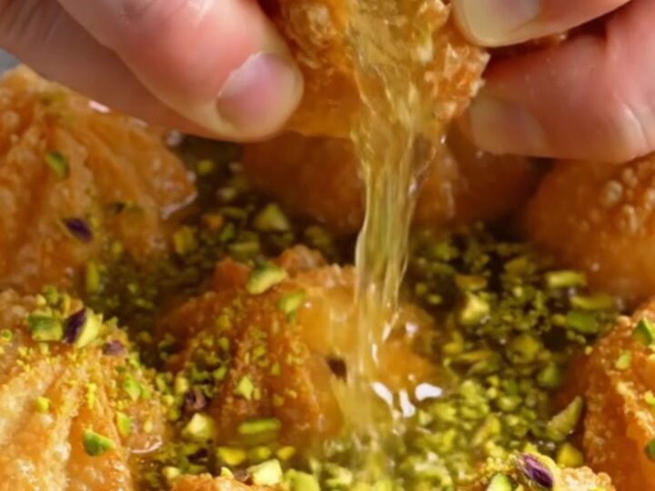 Golden fluted tulumba pastries glistening with syrup and topped with crushed pistachios on a plate