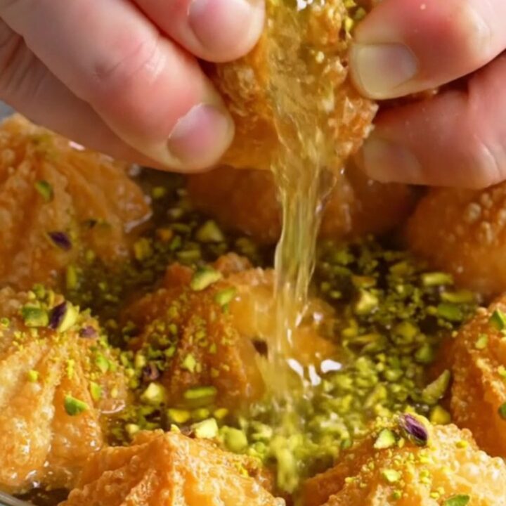 Golden fluted tulumba pastries glistening with syrup and topped with crushed pistachios on a plate