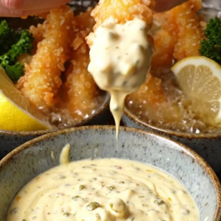 Crispy panko-crusted calamari steak strips piled on a plate with a bowl of lemon caper aioli for dipping.