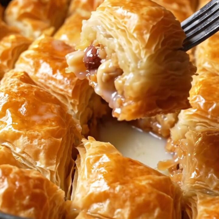 Golden diamond-cut baklava pieces in a baking pan, drizzled with milk syrup and topped with crushed hazelnuts.
