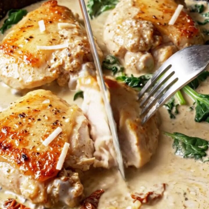 Golden chicken thighs in a creamy Tuscan sauce with sun-dried tomatoes and spinach in a cast iron skillet