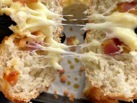 A close-up shot of a warm bread roll being pulled apart, revealing melted mozzarella and crispy beef bacon.
