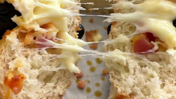 A close-up shot of a warm bread roll being pulled apart, revealing melted mozzarella and crispy beef bacon.
