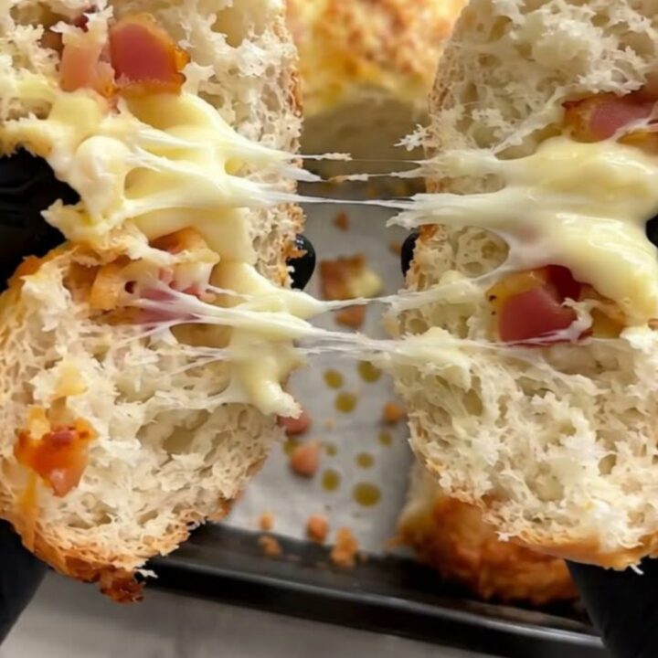 A close-up shot of a warm bread roll being pulled apart, revealing melted mozzarella and crispy beef bacon.