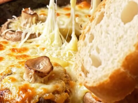 Baked mushroom caps topped with melted, blistered kaşar cheese in a clay dish