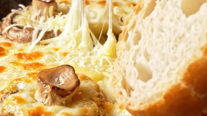 Baked mushroom caps topped with melted, blistered kaşar cheese in a clay dish