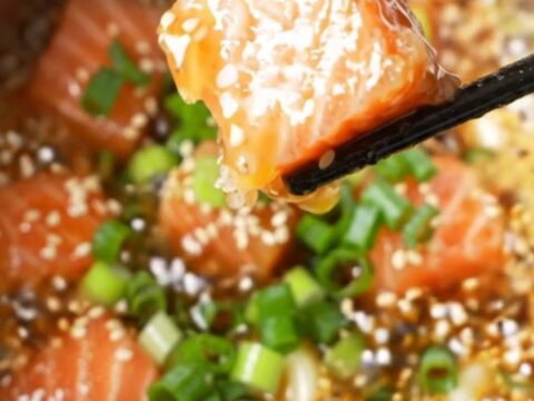 Crispy air-fried salmon cubes coated in sticky honey garlic glaze, sprinkled with sesame seeds and scallions, in a bowl