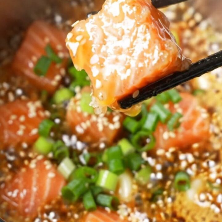 Crispy air-fried salmon cubes coated in sticky honey garlic glaze, sprinkled with sesame seeds and scallions, in a bowl