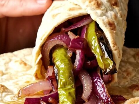 Grilled lamb shish skewers with charred peppers and sumac onions on a plate, with lavash bread.