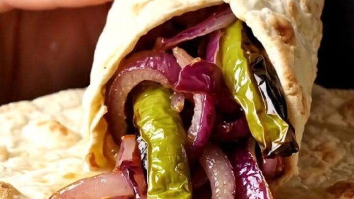 Grilled lamb shish skewers with charred peppers and sumac onions on a plate, with lavash bread.