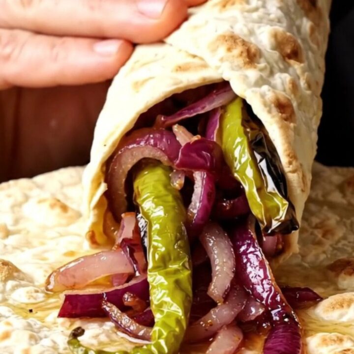 Grilled lamb shish skewers with charred peppers and sumac onions on a plate, with lavash bread.