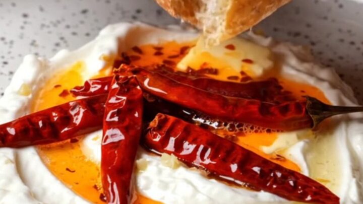 Whipped garlic yogurt topped with sizzling chili butter in a ceramic bowl, with crusty bread on the side.