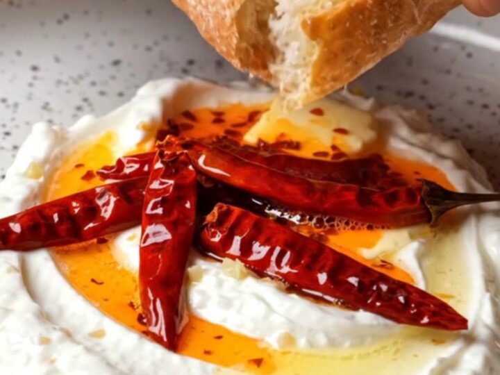 Whipped garlic yogurt topped with sizzling chili butter in a ceramic bowl, with crusty bread on the side.