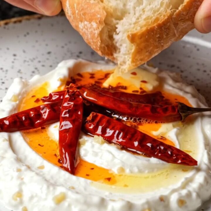 Whipped garlic yogurt topped with sizzling chili butter in a ceramic bowl, with crusty bread on the side.