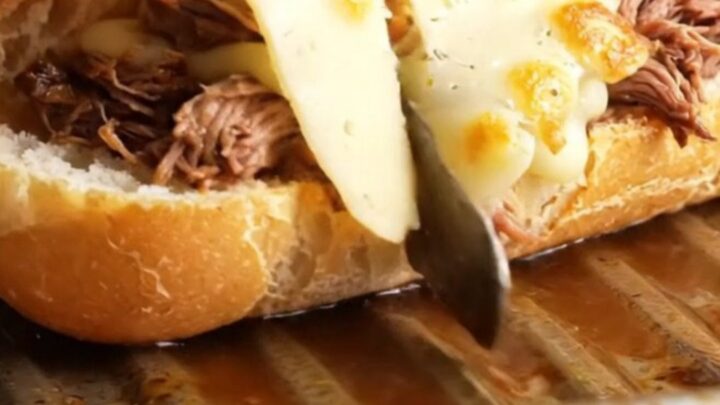 Slow-cooked short rib French dip baguette with melted Gruyère, cut in half, showing juicy beef and cheese