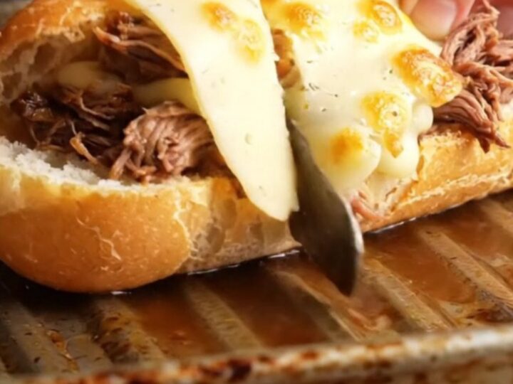 Slow-cooked short rib French dip baguette with melted Gruyère, cut in half, showing juicy beef and cheese