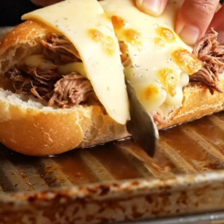 Slow-cooked short rib French dip baguette with melted Gruyère, cut in half, showing juicy beef and cheese