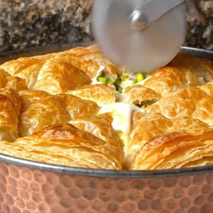 Golden, blistered katmer pastry on a copper pan, with pistachios visible