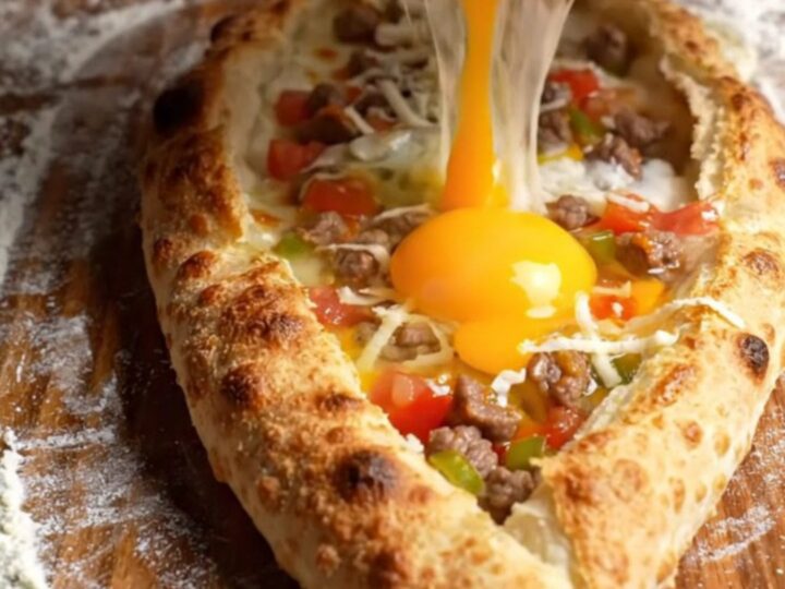 Golden boat-shaped pide with melted cheese and a runny egg yolk, brushed with butter