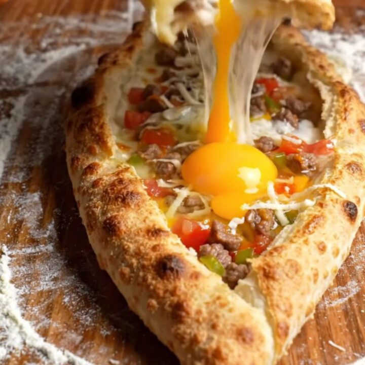 Golden boat-shaped pide with melted cheese and a runny egg yolk, brushed with butter