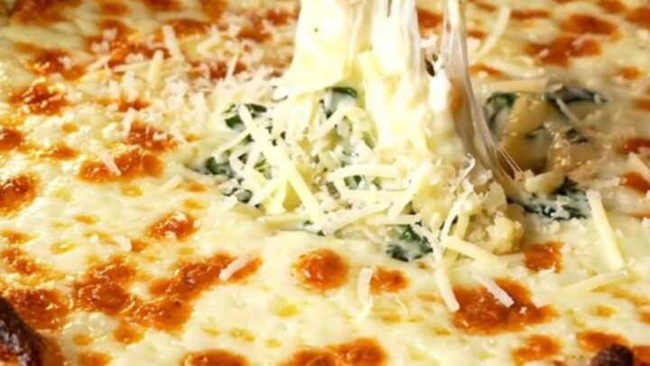 Bubbling cheesy spinach artichoke dip in a cast-iron skillet with golden top and garlic baguette slices