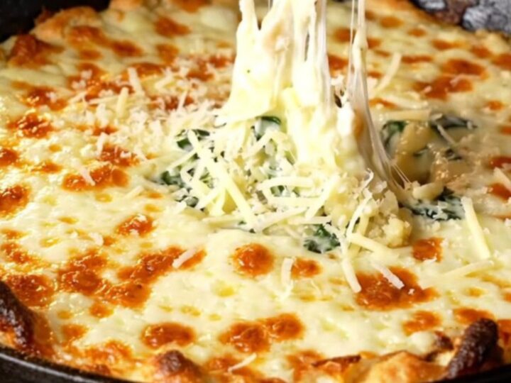 Bubbling cheesy spinach artichoke dip in a cast-iron skillet with golden top and garlic baguette slices