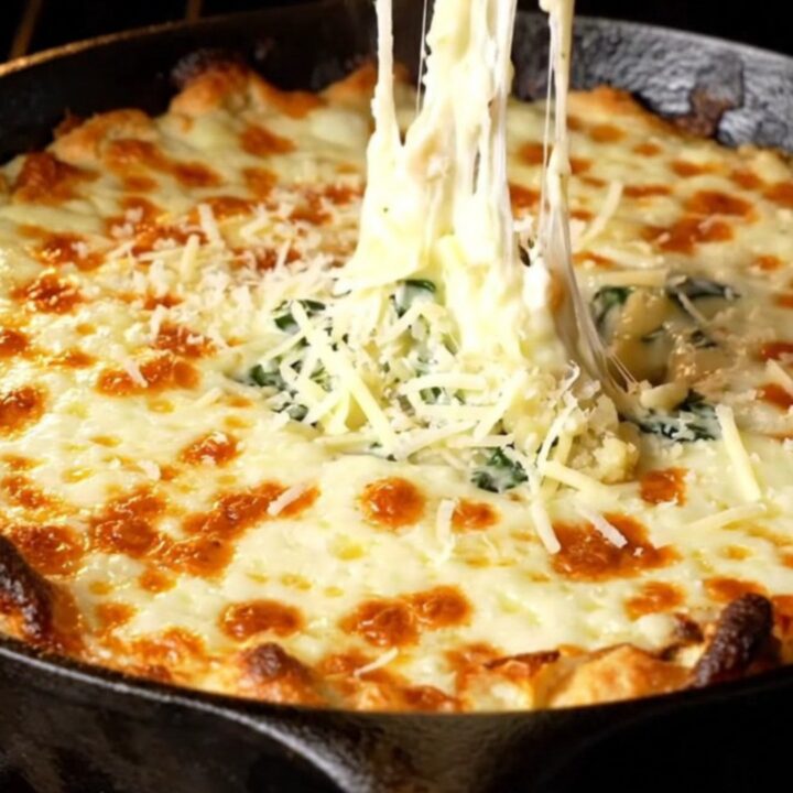 Bubbling cheesy spinach artichoke dip in a cast-iron skillet with golden top and garlic baguette slices