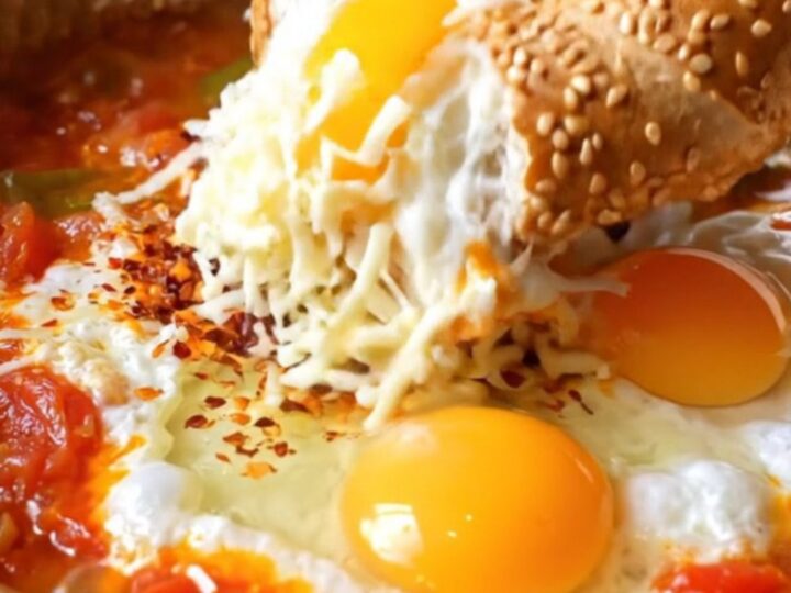 Copper pan of Turkish menemen with melted kaşar cheese and a piece of sesame simit dipping in
