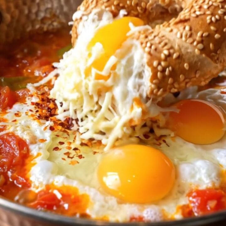 Copper pan of Turkish menemen with melted kaşar cheese and a piece of sesame simit dipping in