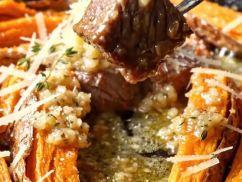 A cast iron skillet with crispy accordion sweet potatoes and seared steak cubes in garlic butter