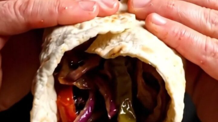 Sizzling Adana kebab on a wide skewer being slid onto warm lavash with charred tomatoes and sumac onions.