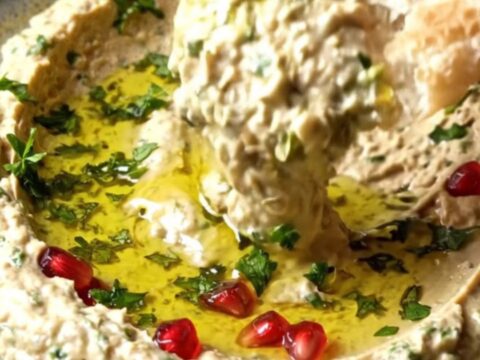 Bowl of smoky Turkish babaganoush topped with pomegranate seeds and a swirl of olive oil, with pita bread on the side.