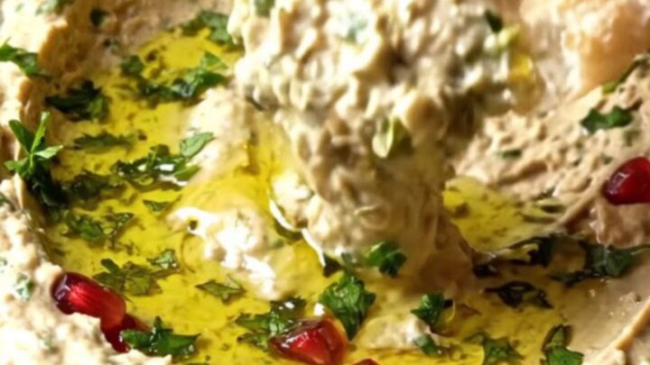 Bowl of smoky Turkish babaganoush topped with pomegranate seeds and a swirl of olive oil, with pita bread on the side.