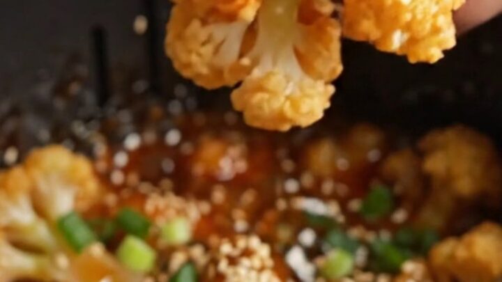 Crispy air-fried sticky sesame cauliflower wings in a bowl, coated in glossy glaze with sesame seeds and scallions