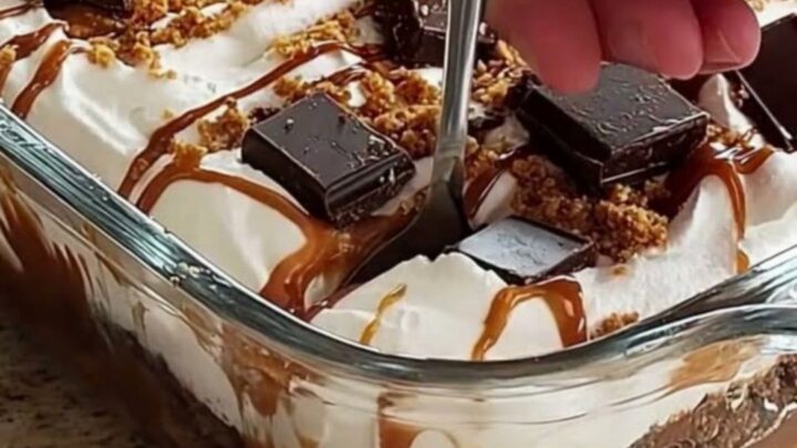 A clear glass dish filled with layers of white whipped cream, amber caramel, and dark chocolate chunks.