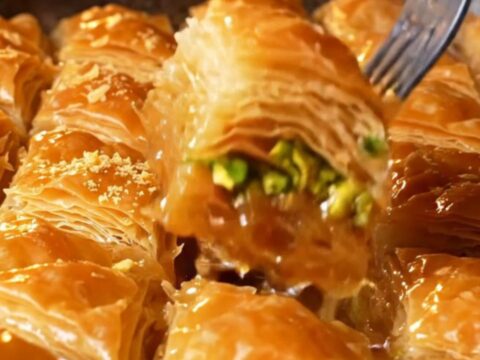 Golden diamond-cut baklava with pistachios and syrup being poured over