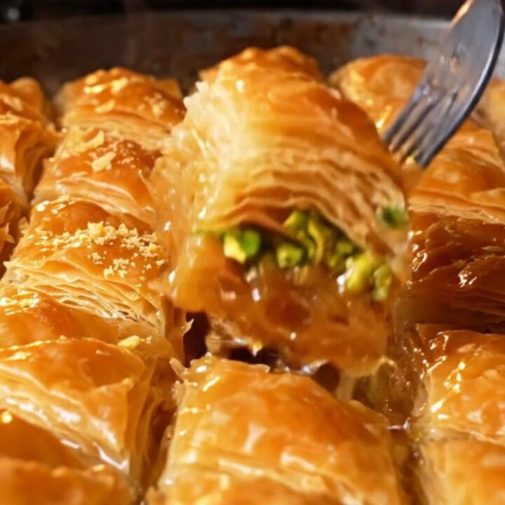Golden diamond-cut baklava with pistachios and syrup being poured over