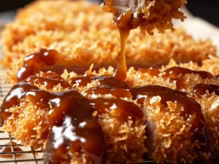 Sliced tonkatsu cutlet with crispy panko crust and juicy pork, drizzled with sauce, served with rice and cabbage