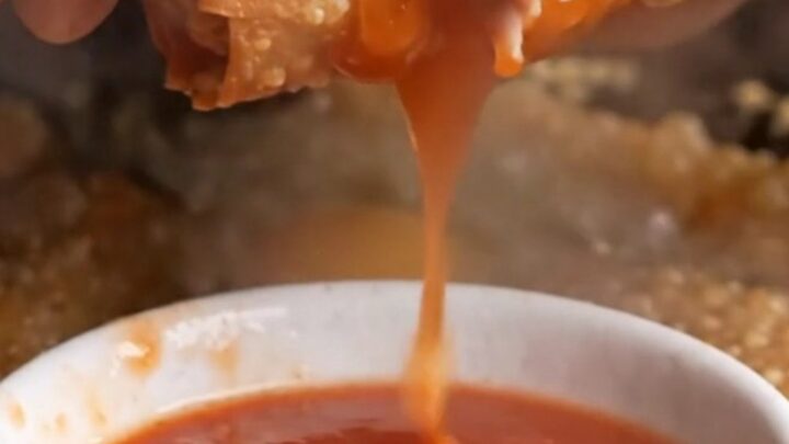 Crispy rice paper egg rolls with blistered golden crust, served with sweet plum sauce in a small bowl.