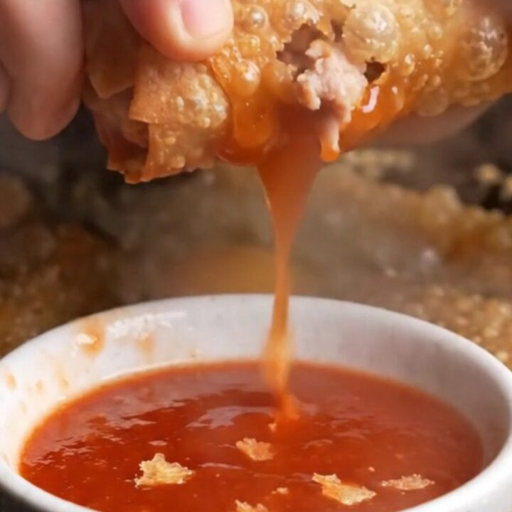 Crispy rice paper egg rolls with blistered golden crust, served with sweet plum sauce in a small bowl.