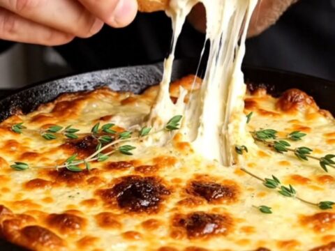 A cast iron skillet filled with bubbling French onion dip, topped with melted Gruyère and garnished with fresh thyme