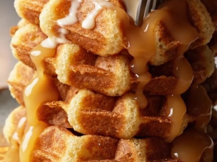 Stack of golden churro waffles topped with vanilla ice cream and warm dulce de leche cascading down the sides.