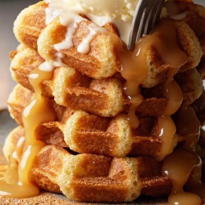 Stack of golden churro waffles topped with vanilla ice cream and warm dulce de leche cascading down the sides.
