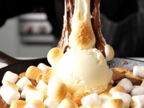 Giant s'mores skillet cookie with golden toasted marshmallows and melted chocolate in a cast iron skillet